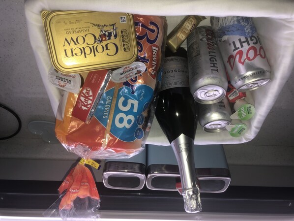Ein Kühlschrank mit verschiedenen Lebensmitteln, darunter eine Weinflasche, Bierdosen und einer Packung Snacks.