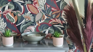 En trappe med væg i blomstermønster, et gråt skab med to potteplanter, en skål og en vase med tørrede planter.