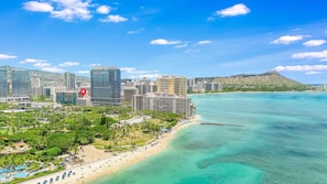 A coastal cityscape with a prominent hotel featuring a large red pin icon, indicating its location.