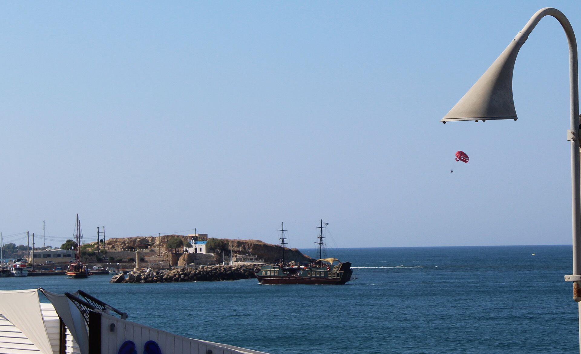 Escena costera con un barco amarrado en el muelle, un faro y un cielo azul despejado.