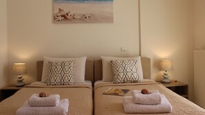 Camera d'albergo con due letti, ognuno con cuscini e asciugamani decorati. Sopra i letti, un quadro a tema spiaggia.