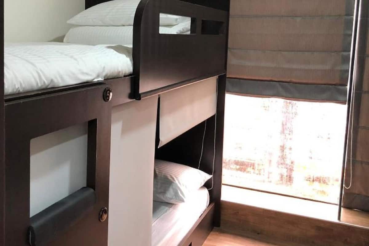Een stapelbed met een raam, houten vloer en een gordijn.
