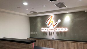 Un taulell de recepció d'hotel amb un disseny modern, un logotip a sobre del taulell i una paret amb un rètol en una llengua estrangera.