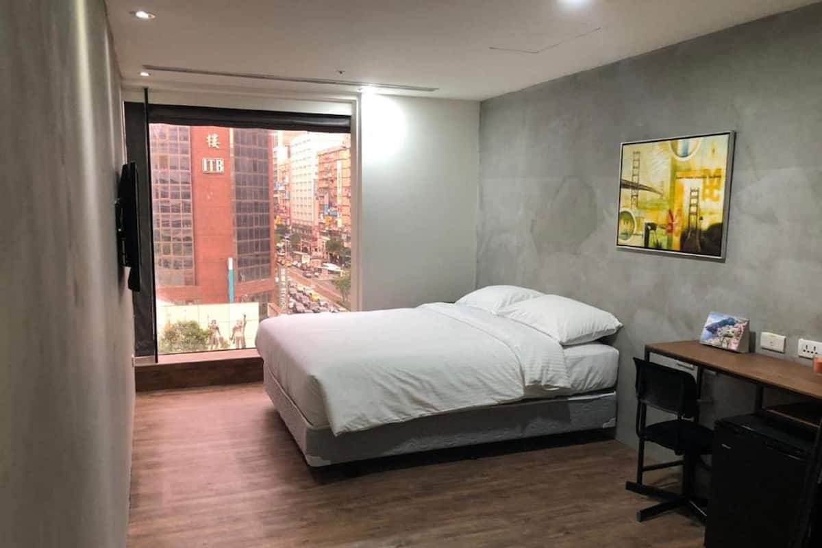 Een moderne slaapkamer met een bed, een bureau en uitzicht op een stadsbeeld door een glazen deur.