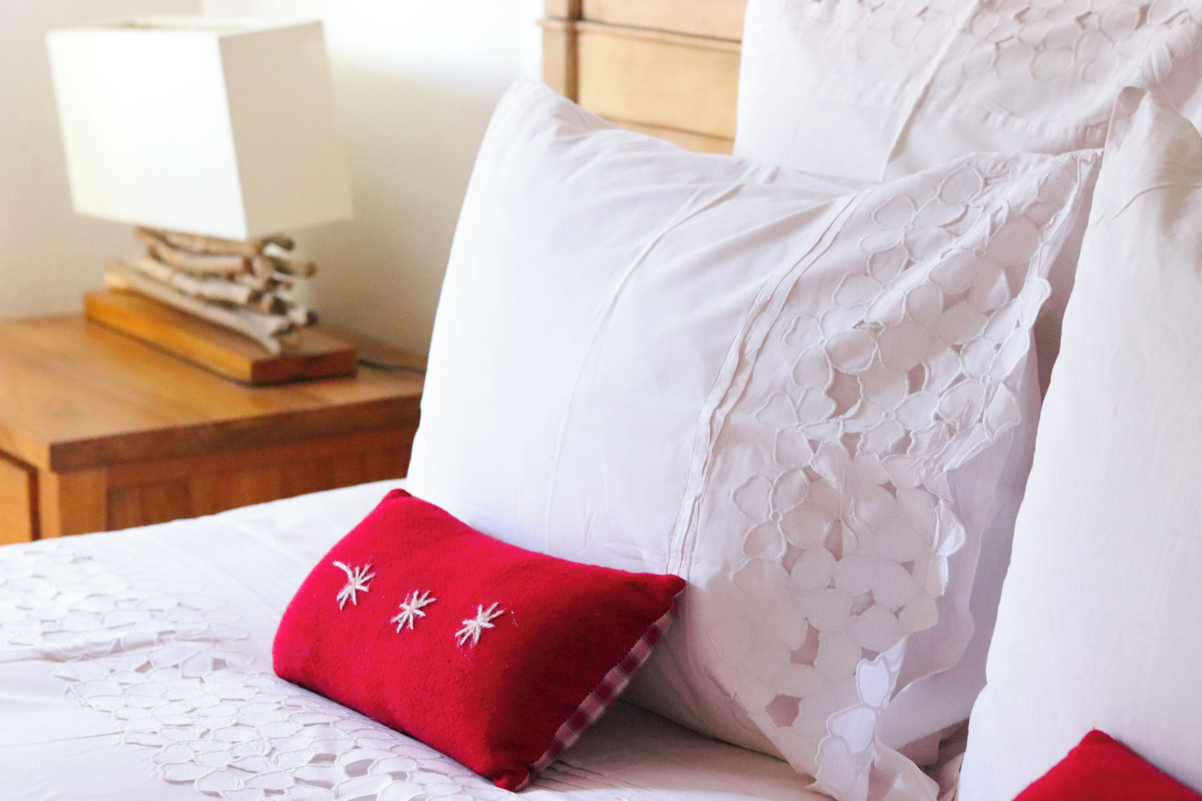 A neatly made bed with white linens and a red pillow with a snowflake design.