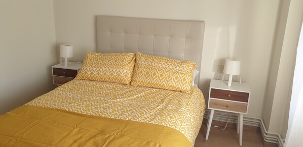 A neatly made bed with a patterned bedspread and pillows, a bedside table with a lamp, and a nightstand with a lamp.