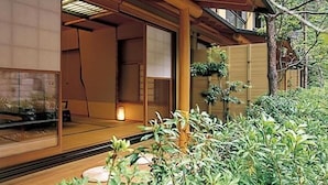 A traditional Japanese-style room with tatami flooring, sliding doors, and a view of a garden with plants and a tree. - Nishiyama Onsen Keiunkan (Hayakawa)