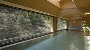 A spacious indoor area with a large window offering a view of a forested landscape. - Nishiyama Onsen Keiunkan (Hayakawa)