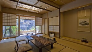 A traditional Japanese room with tatami flooring, a low table, a cushioned chair, sliding doors, and a framed picture on the wall. - Nishiyama Onsen Keiunkan (Hayakawa)