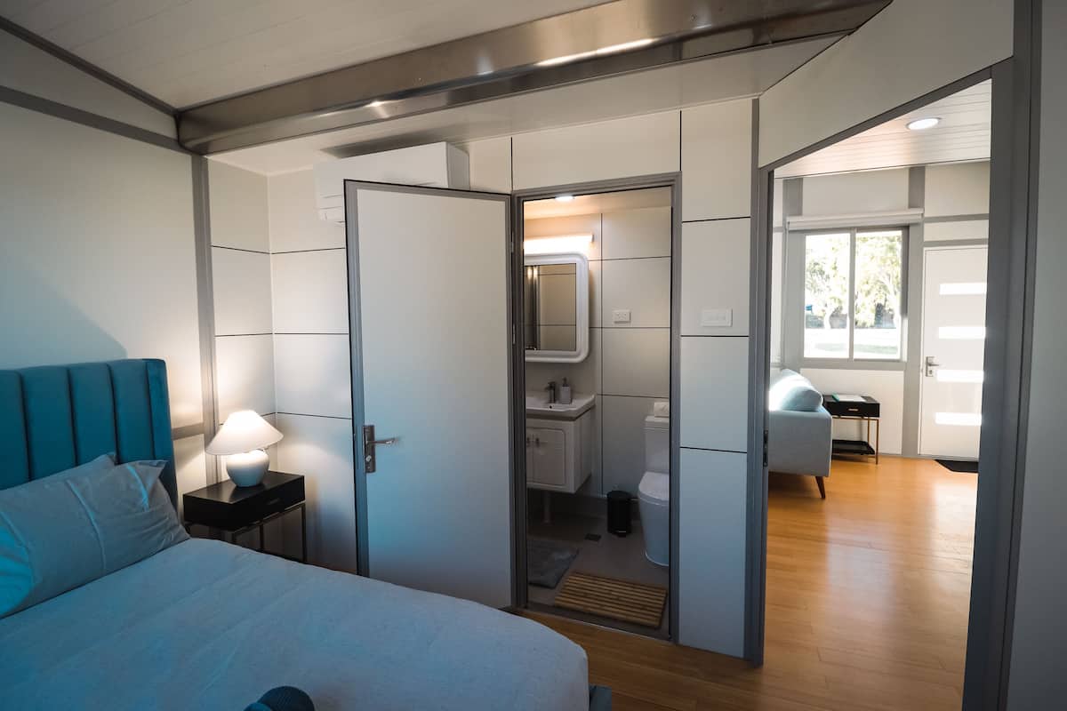 Una habitación de hotel moderna con una cama, una mesita de noche y un baño visible a través de un panel de vidrio.