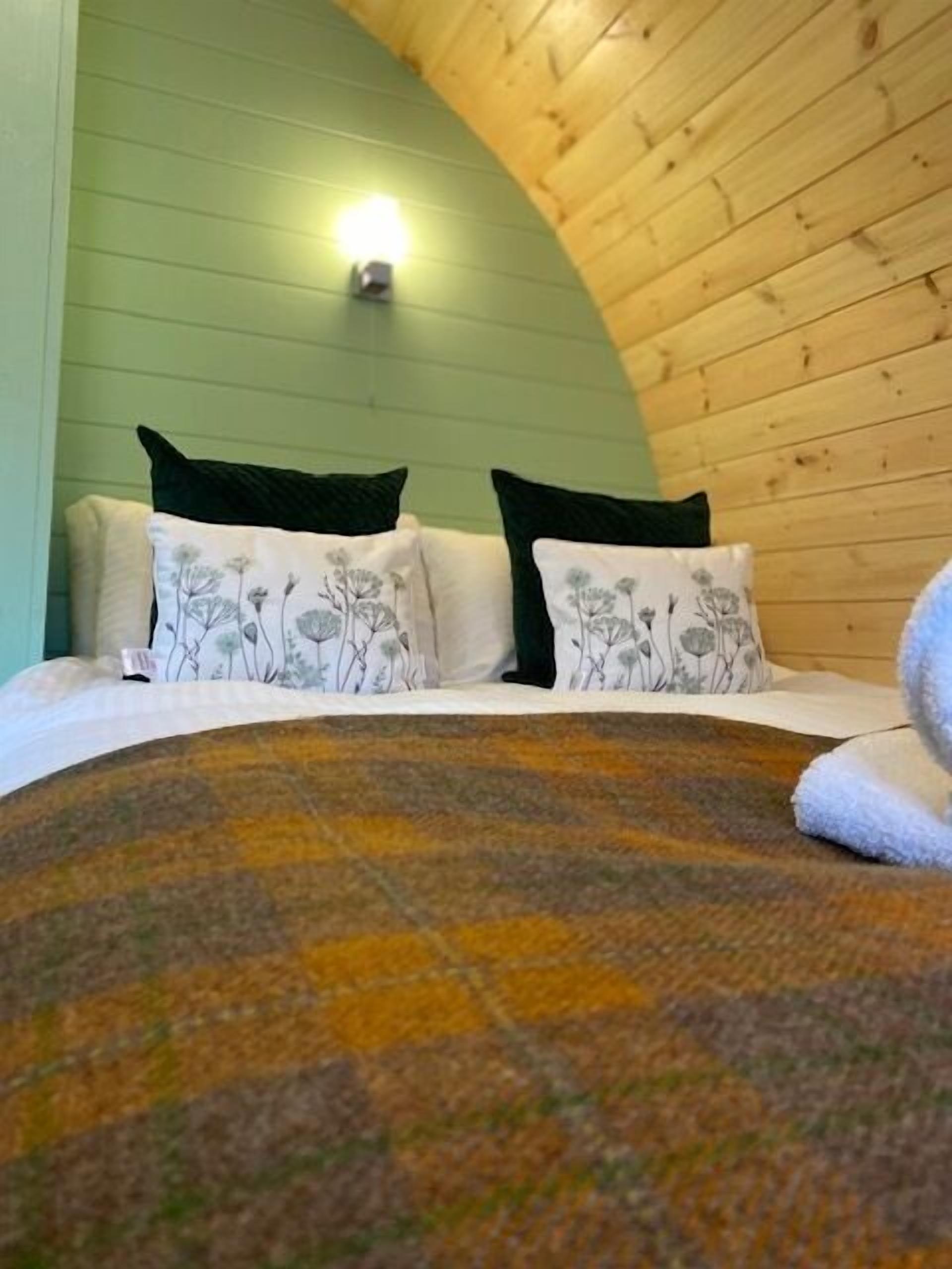 Une pièce chaleureuse avec un plafond en bois aux lignes courbes, un lit agrémenté d’oreillers à motifs floraux et une couverture.