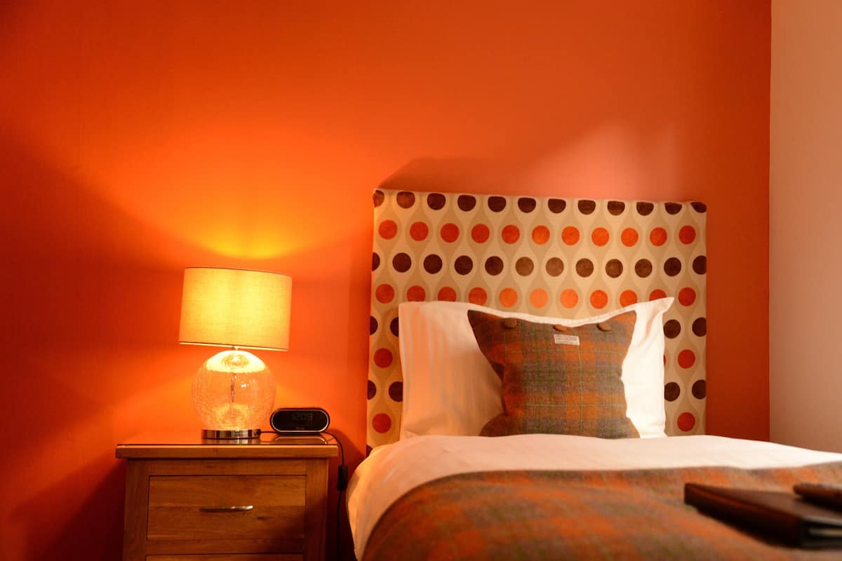 Una habitación de hotel con una cama, una mesita de noche, una lámpara y un reloj digital.