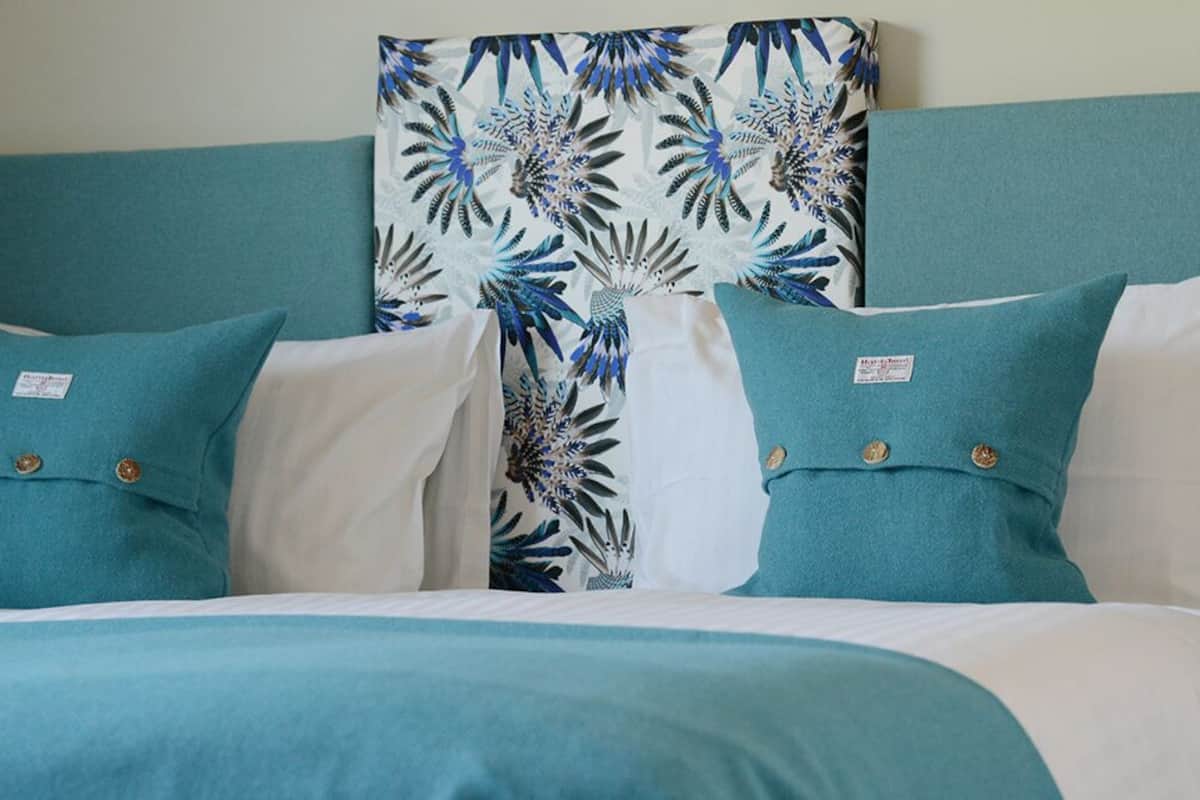 Una cama con ropa de cama verde aguamarina y blanca, un cabecero verde aguamarina y un muro con estampado floral.
