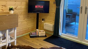 A cozy room with a wooden ceiling, a television displaying 'NETFLIX', a small table with a plant, and a view of a mountainous landscape through a glass door. - Torlinnhe Guesthouse (Fort William)