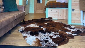 A cozy cabin interior with a wooden ceiling, a sofa, a cowhide rug, a bed, and a kitchenette. - Torlinnhe Guesthouse (Fort William)