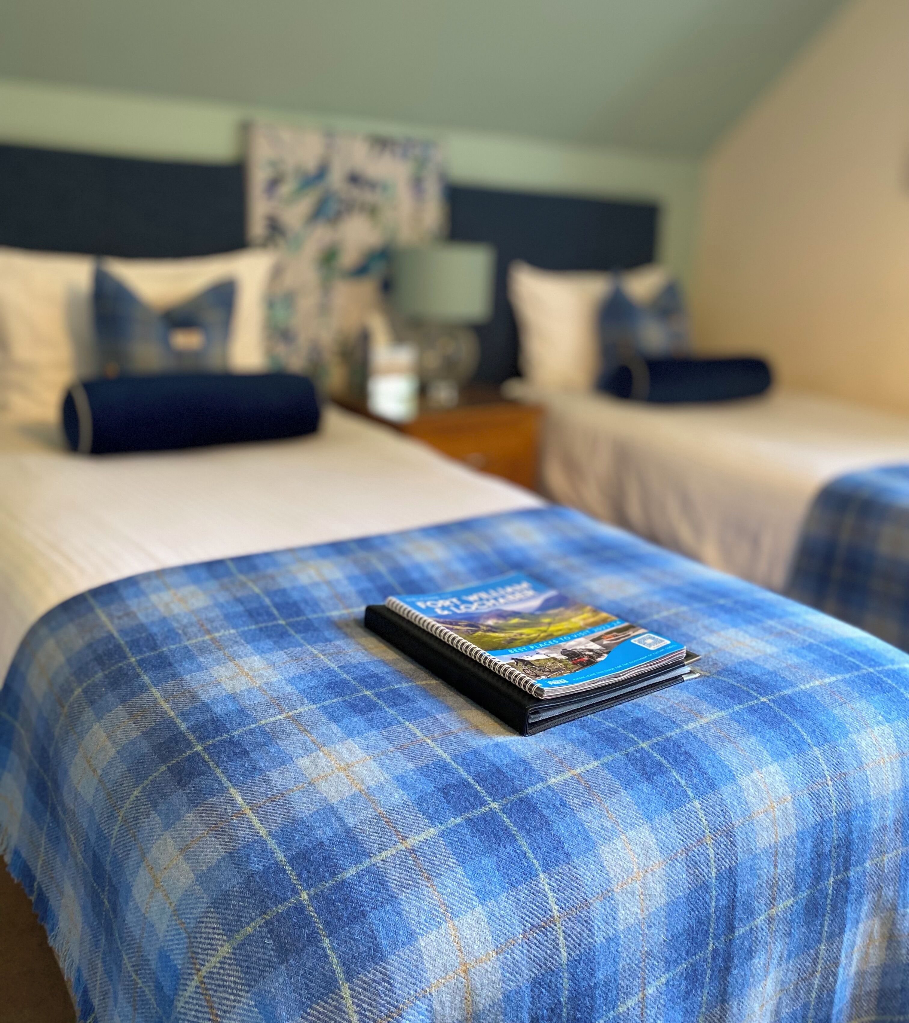 Habitación de hotel con dos camas, cada una con una colcha azul a cuadros y una revista sobre la cama de la izquierda.