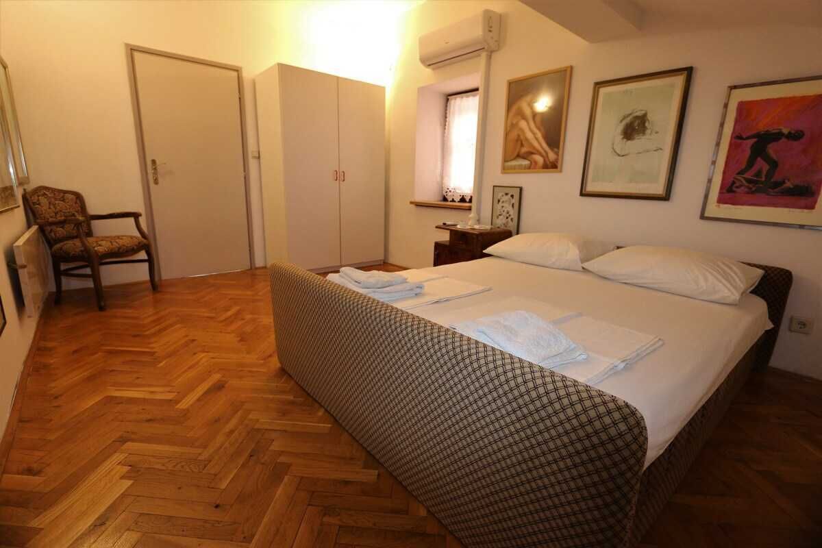 Ein Schlafzimmer mit Bett, Sessel, Kleiderschrank und einem Fenster mit Vorhängen.
