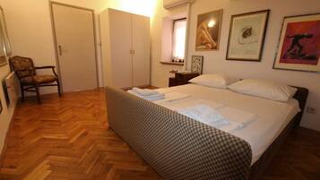Ein Schlafzimmer mit Bett, Sessel, Kleiderschrank und einem Fenster mit Vorhängen.
