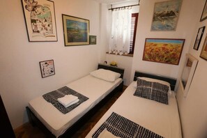 A small, clean room with two single beds, a window with curtains, and various framed pictures on the walls. - Apartment Ljustina (Silo - island Krk)