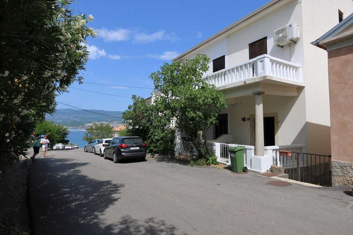 Rua residencial com carros estacionados, uma varanda e vista para o mar.