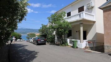 Rua residencial com carros estacionados, uma varanda e vista para o mar.