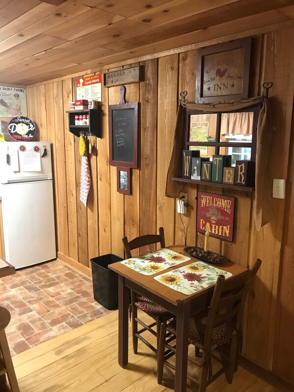 L’intérieur d’un chalet en bois, avec une table à manger, des chaises, un réfrigérateur, un tableau noir servant de menu et une pancarte indiquant « Bienvenue dans notre chalet ».