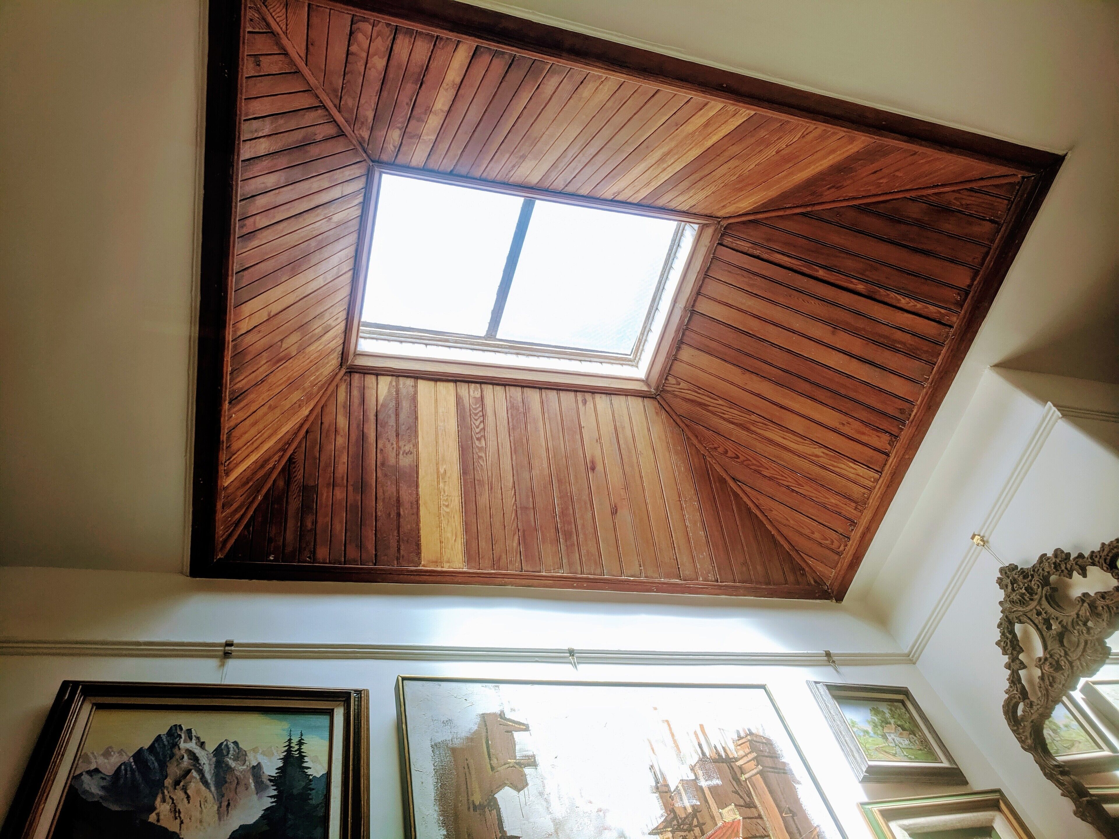 A room with a sloped wooden ceiling and a skylight. There are framed pictures on the wall.