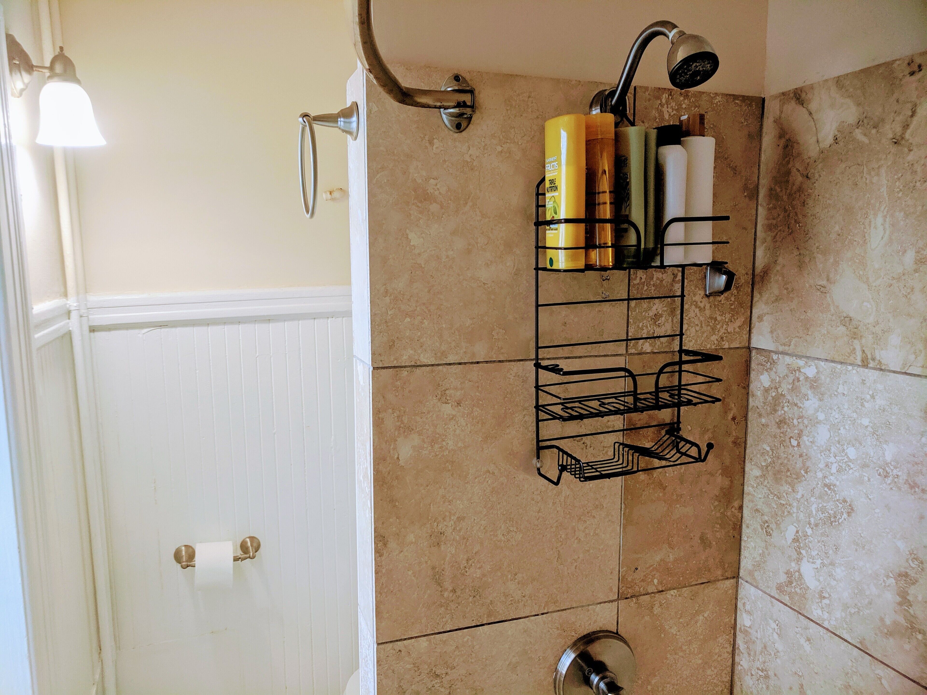 A bathroom with a shower, a towel rack, and toiletries on a shelf.
