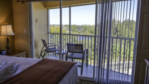Una camera d'hotel con un letto, una sedia, un tavolo e un balcone affacciato su alberi e palazzi.