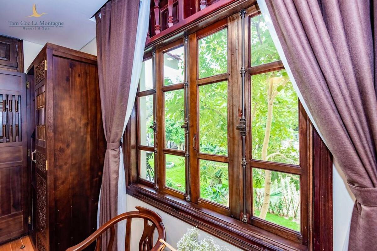 A room with a large window, wooden furniture, and a view of greenery outside.
