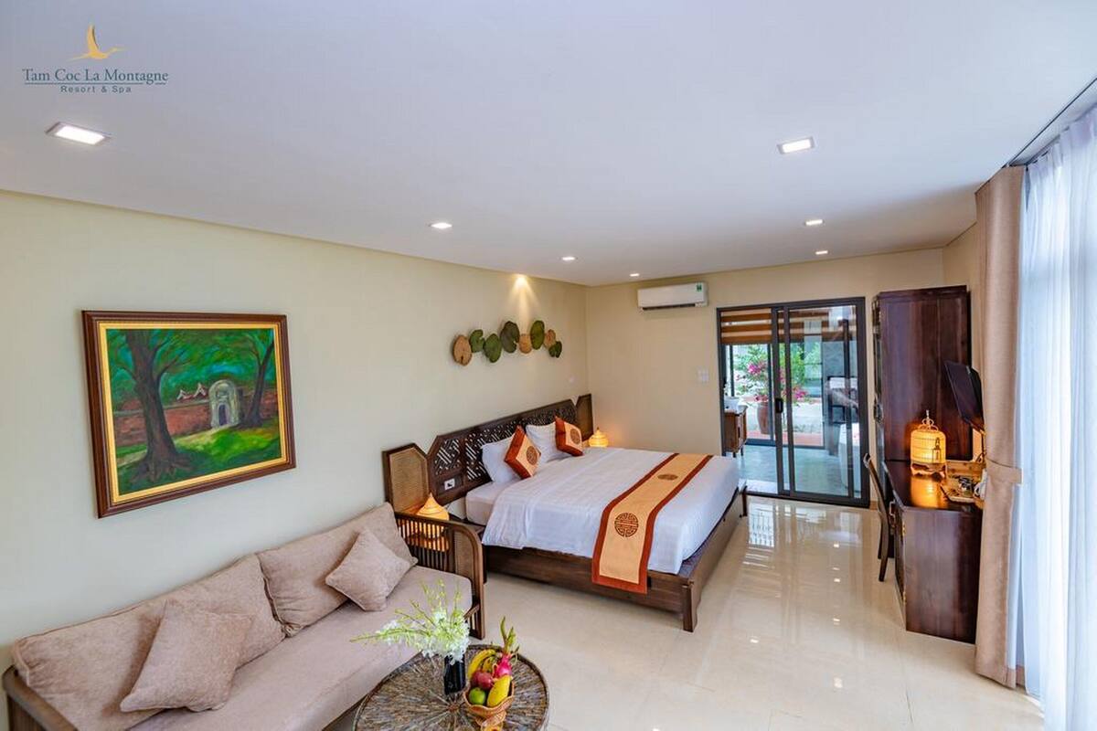 A hotel room with a bed, a sofa, a small table with fruit, and a painting on the wall.