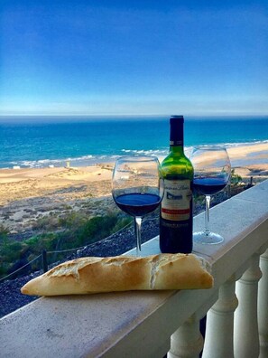 Una botella de vino y dos copas en un balcón con vista al océano.