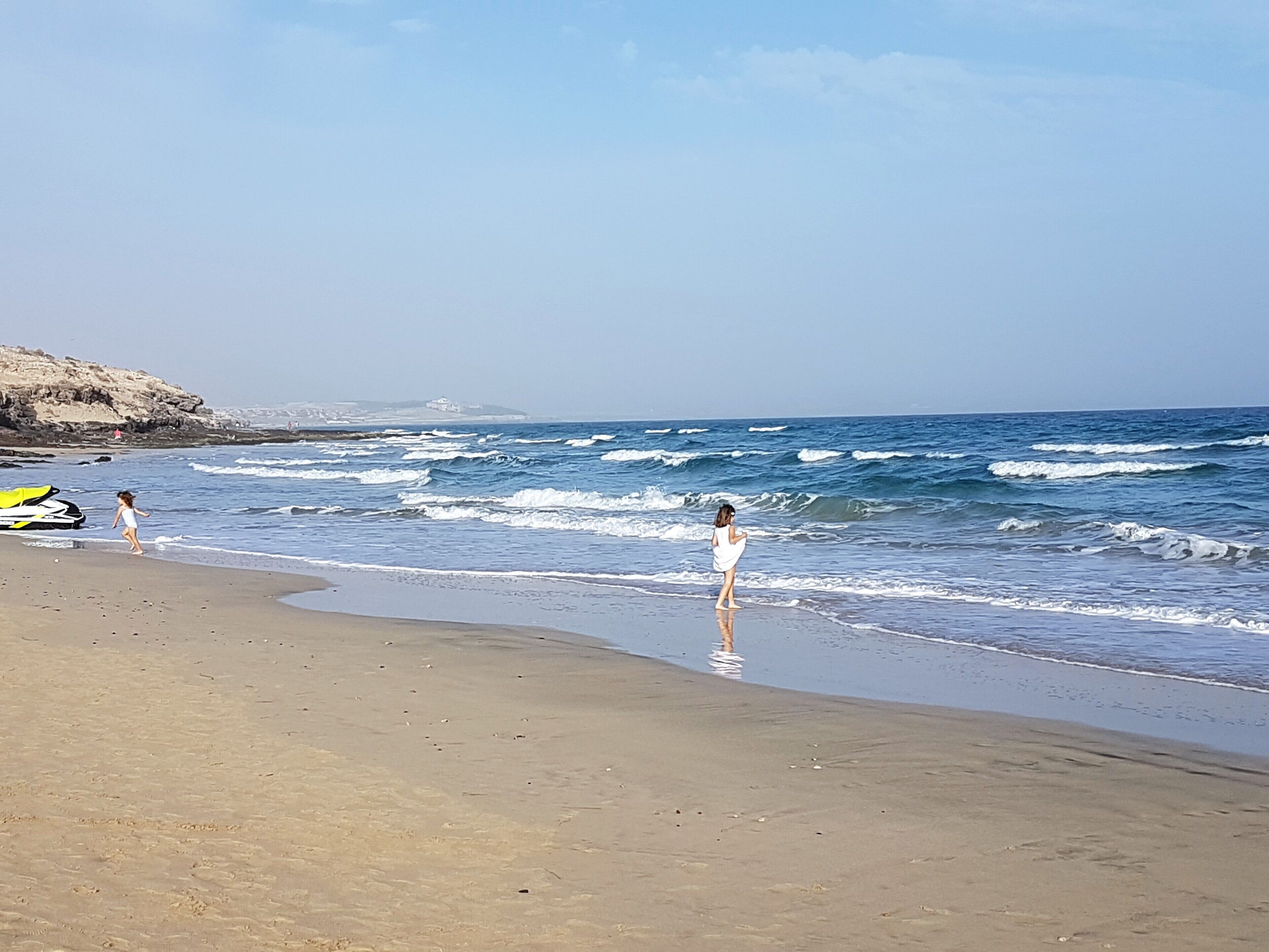 A beach with a rocky cliff and a surfboard.