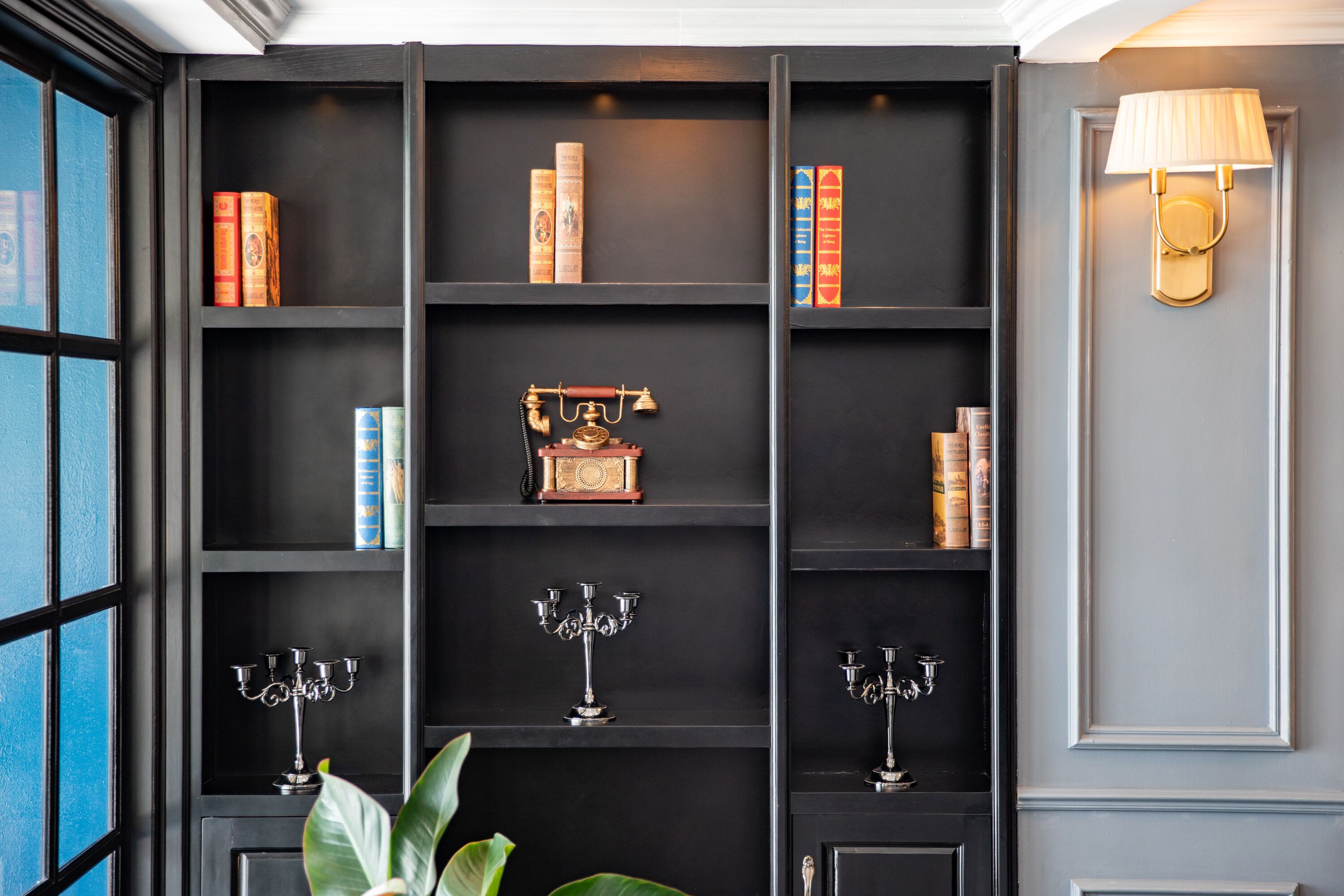 A bookshelf with books and decorative items, a lamp, and a plant.