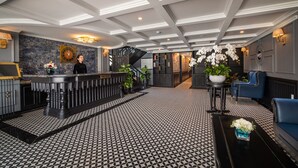 Un vestíbul amb un paviment de disseny en blanc i negre, una recepció, una escala i zones d'estar.
