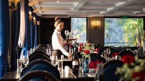 Un restaurant amb taules preparades per dinar, un cambrer ates als clients i vistes a la verdor exterior.