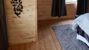 Une cabane en bois avec un plafond en pente, un élément décoratif mural, un lit et une fenêtre avec des rideaux.