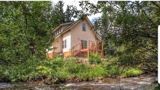 Une maison dotée d’une terrasse donnant sur un ruisseau, entourée d’une végétation luxuriante.
