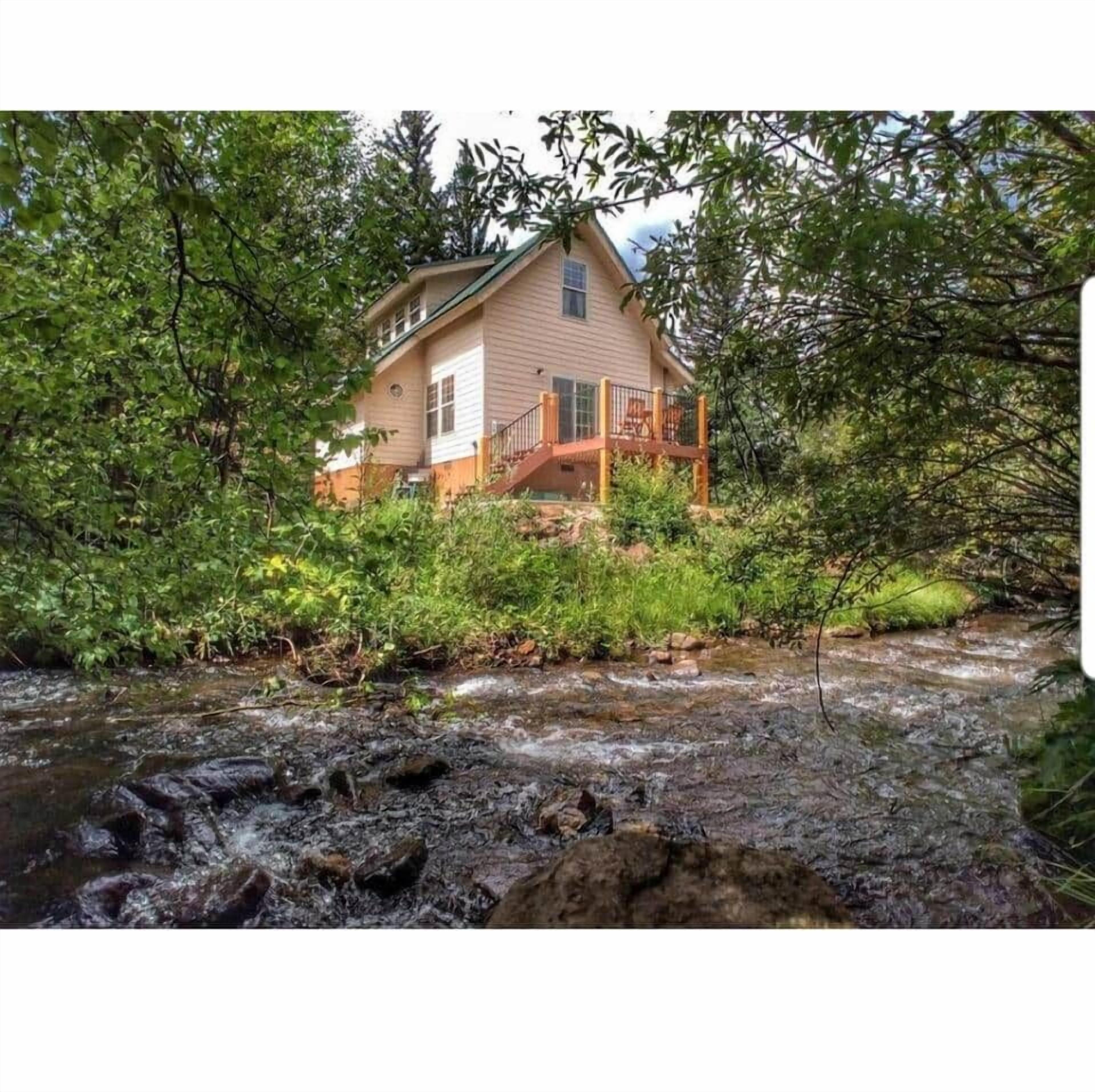 Ett hus med en veranda som vetter ut mot en bäck, omgivet av tät grönska.