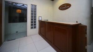 A hotel reception area with a wooden reception desk, a glass door with a window, and a sign that reads "HOTEL London Since 1975". - Hotel O London (Sandakan)
