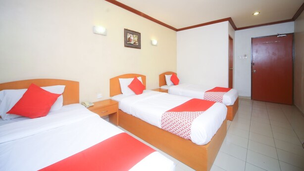A hotel room with three single beds, each with a red and white bedspread, wooden headboards, and bedside tables with lamps. - Hotel O London (Sandakan)
