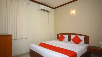 A hotel room with a bed, a nightstand, an air conditioning unit, and a wall-mounted light.
