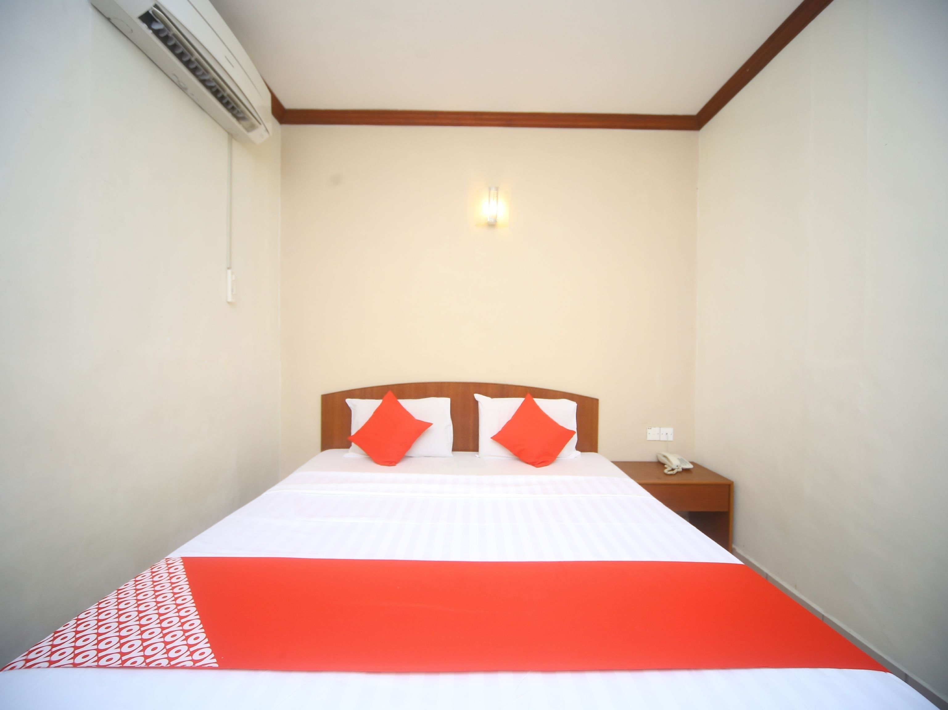 Una habitación de hotel con cama, mesita de noche, lámpara de pared y equipo de aire acondicionado.
