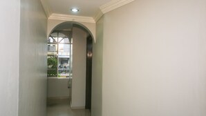 A hallway with a tiled floor, a white wall, and a window with a view of buildings outside. - Hotel O London (Sandakan)