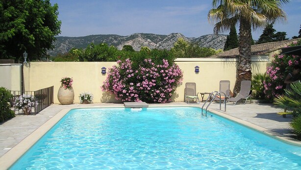 Une piscine avec vue sur les montagnes en arrière-plan, entourée de verdure et agrémentée de quelques chaises.
