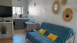 Un salon avec un canapé bleu, des coussins jaunes, une petite table ronde et un téléviseur.