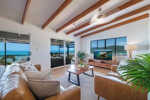 Ein geräumiges Wohnzimmer mit großem Fernseher, bequemen Sitzmöglichkeiten und einem Balkon mit Blick.