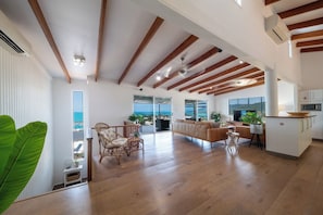 A spacious living area with wooden beams, a kitchen, and a view of the ocean. - Nautilus On The Hill - Luxury Holiday Home in Central Airlie (Airlie Beach)