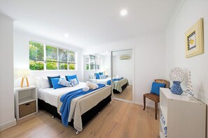 Ein Schlafzimmer mit zwei Betten, einem Spiegel, einem Stuhl, einer Lampe und einer Kommode.