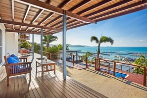 A wooden deck with outdoor furniture, a pool, and a view of the marina and ocean.